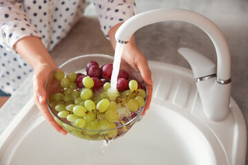 Woman washing fresh grapes in kitchen sink, closeup