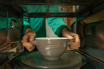 Women's hands take a plate out of the microwave, photo from inside