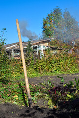 Shovel in the ground and garden beds with smoke from chimney