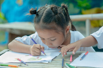 Cute cheerful child drawing using a pencil drawingwhile sitting at the table,Girl drawing and learning with educator