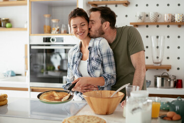 Husband and wife making pancakes at home. Loving couple having fun while cooking