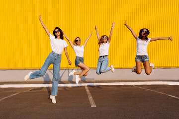 Excited happy group of friends having fun and jumping against yellow wall background on sunny...