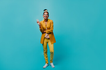 Fototapeta na wymiar Slim african girl in yellow costume posing with smile. Spectacular black female model standing on blue background.