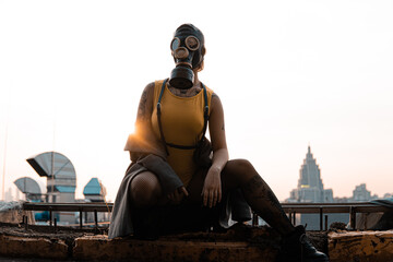 A girl in a gas mask, coat and body sits on the background of the city