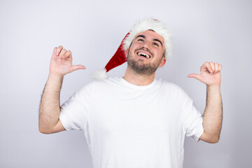 Young handsome man wearing a Santa hat over white background looking confident with smile on face,...