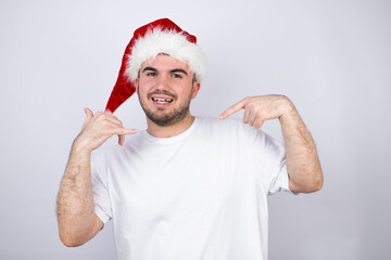 Young handsome man wearing a Santa hat over white background doing the “call me” gesture with her hands.