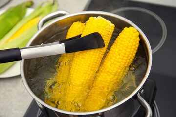 Taking boiled corn from pot with tongs in kitchen, closeup