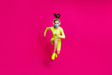 Fototapeta na wymiar Full length body size photo of female runner jumping high running fast wearing covid-19 mask isolated on vibrant fuchsia color background