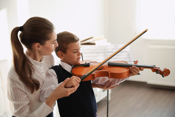 Young woman teaching little boy to play violin indoors © New Africa