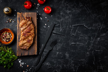 Grilled beef steak on a board with spices on a black background, free space for text