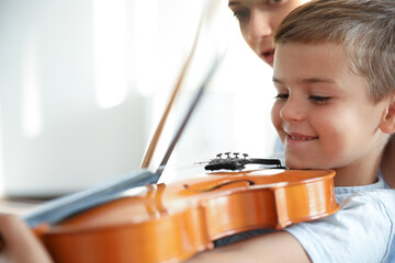 Young woman teaching little boy to play violin indoors, closeup
