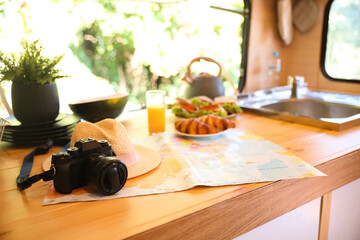 Camera, hat and world map on wooden table in modern trailer. Camping vacation