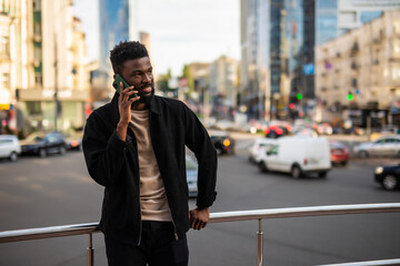 Handsome young Afro American businessman is talking on the mobile phone and smiling while standing outdoors