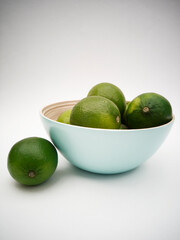 Light blue bowl with green limes on the white background. Juicy colorful fruits for mojito. Freshness and health.