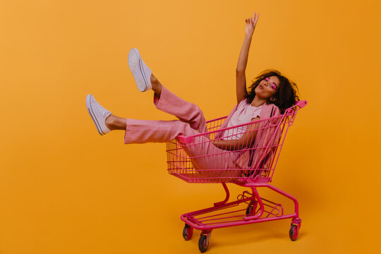 Enthusiastic brunette girl expressing sincere positive emotions. Studio shot of beautiful woman sitting in shopping cart.