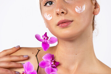 Beauty portrait. Girl with cream on her cheeks, making the skin softer and more hydrated. In hands with an orchid. Skin care concept