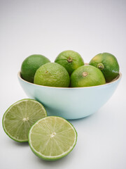 Light blue bowl with limes inside and a lime cut in half on the white background. Juicy, fresh and colorful fruits.