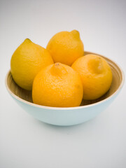 Light blue bowl with yellow lemons inside and a lemon next to it on the white background. Juicy, fresh and colorful fruits.