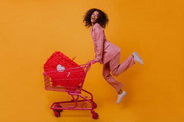 Enthusiastic shopaholic girl jumping on yellow background. Trendy african woman posing with...