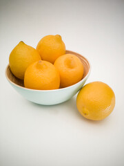 Light blue bowl with yellow lemons inside and a lemon next to it on the white background. Juicy, fresh and colorful fruits.