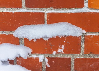 Snow stuck to the wall of a red brick building close-up in winter