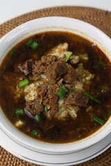 Rawon, Indonesian traditional beef soup from Java Island. Served on white ceramic bowl topped with onion cracker and spring onion,chili paste and lime slices on rattan matt. Isolated white background.