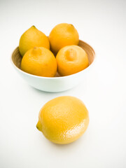 Light blue bowl with yellow lemons inside and a lemon next to it on the white background. Juicy, fresh and colorful fruits.