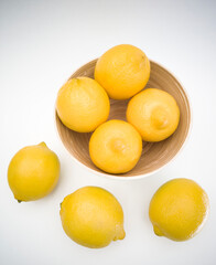 Top view of bamboo bowl with yellow lemons inside and lemons next to it on the white background. Juicy, fresh and colorful fruits.