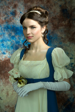 Beautiful girl in a historical dress in the Empire style of the early 19th century on an unusual blue background with streaks and flowers