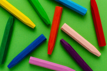 Top view of colorful wax pencils on the bright green surface as a background