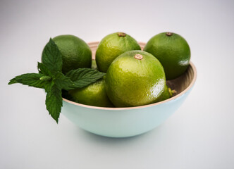 Light blue bowl with green limes and mint leafs inside on the white background. Juicy colorful fruits for mojito. Freshness and health.
