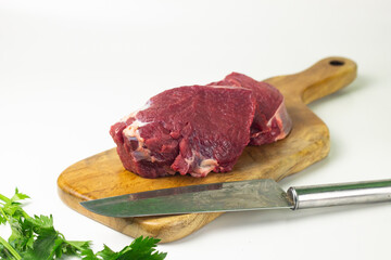 Close of view of slices fresh beef on wooden brown plate, with green celery and spring onion. White isolated background. 