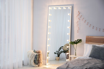 Full length dressing mirror with lamps in stylish bedroom interior