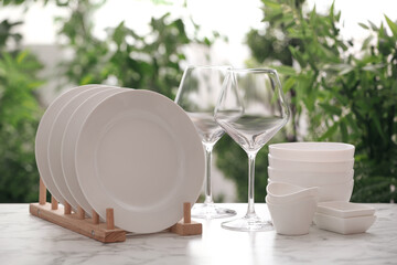 Set of clean dishware and wineglasses on white table against blurred background