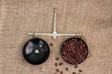 Roasted coffee beans, weighed on an antique hand scale with weights, lying on a table covered with burlap.