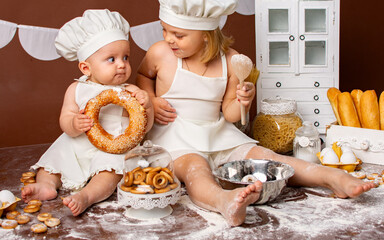 two little girls sisters in chef costumes in the studio with bakery products. The chef plays in the studio.