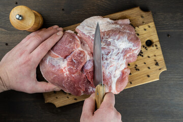 The cook cuts a juicy raw piece of meat on a wooden Board. The view from the top.