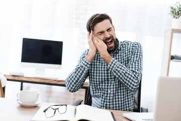 A man in shirt sits and screams from severe pain.