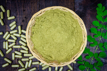 Close-up Moringa powder in wicker basket and Moringa fresh green leaves and capsules on wooden background.