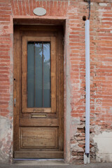 Wooden brown vintage door in the brick building wall. Old cracked brick wall.