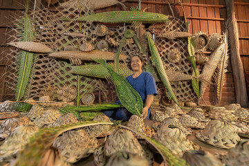 Old Asian woman making Thai local woven straw hat or cap from leaves from natural palm trees product, Thailand. Weaving in market. Old traditional lifestyle. Handmade.