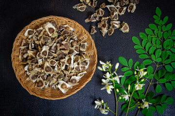 Moringa seeds in wicker baskets, fresh green leaves and Moringa flower on wooden background.