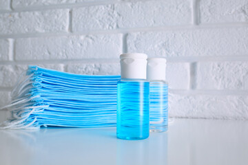 Hand sanitizers and respiratory masks on table near white brick wall. Protective essentials during COVID-19 pandemic