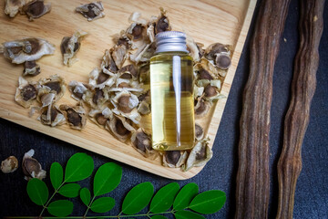 Oil of Moringa in bottle, green leaves, pods and seeds on wooden background. Moringa oleifera tropical herb product concept. 