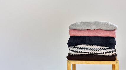 Autumn winter season knitwear. A stack of warm knitted sweaters with different knitting patterns on light gray backgound. Pastel colors. Space for text.