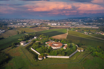 Fototapeta na wymiar Forte Ardietti rises between the territories of Peschiera del Garda and Ponti sul Mincio, Italy. Aerial view of the fortress surrounded by vineyards. Pink clouds at sunset.