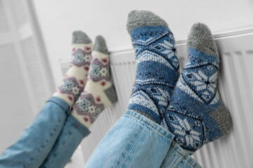 Couple warming legs on heating radiator near white wall, closeup