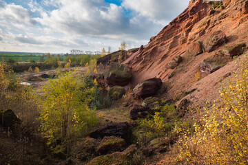 Red mountains with autumn trees and blue cloudy sky. Colored waste heaps after extracting coal from...