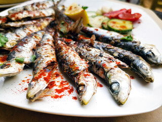 Fresh Grilled sardines served with fresh tomatoes, cucumbers slices and lemon on white plate for mediterranean healthy meal