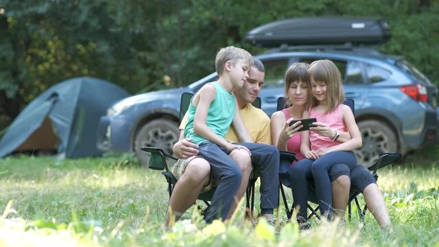 Happy young family resting together at campsite and taking selfie picture with mobile phone camera.